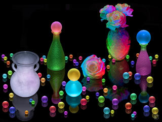 A fine art light painting still life photograph on a black reflective background featuring four glowing vases including a white urn, green bottle with pink orbs